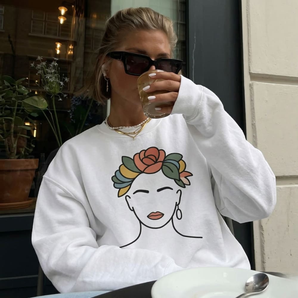 Person wearing a white sweatshirt with a face design, drinking from a glass.
