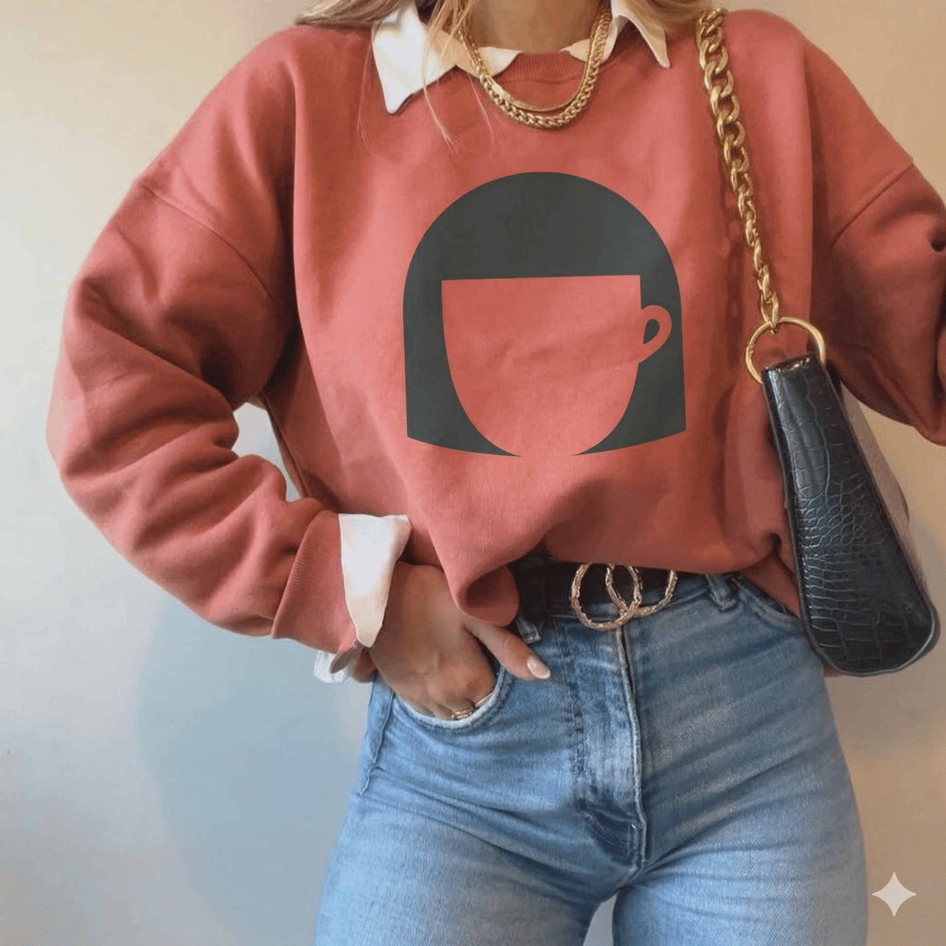Person wearing a pink sweatshirt with a coffee cup design, blue jeans, and carrying a black handbag.