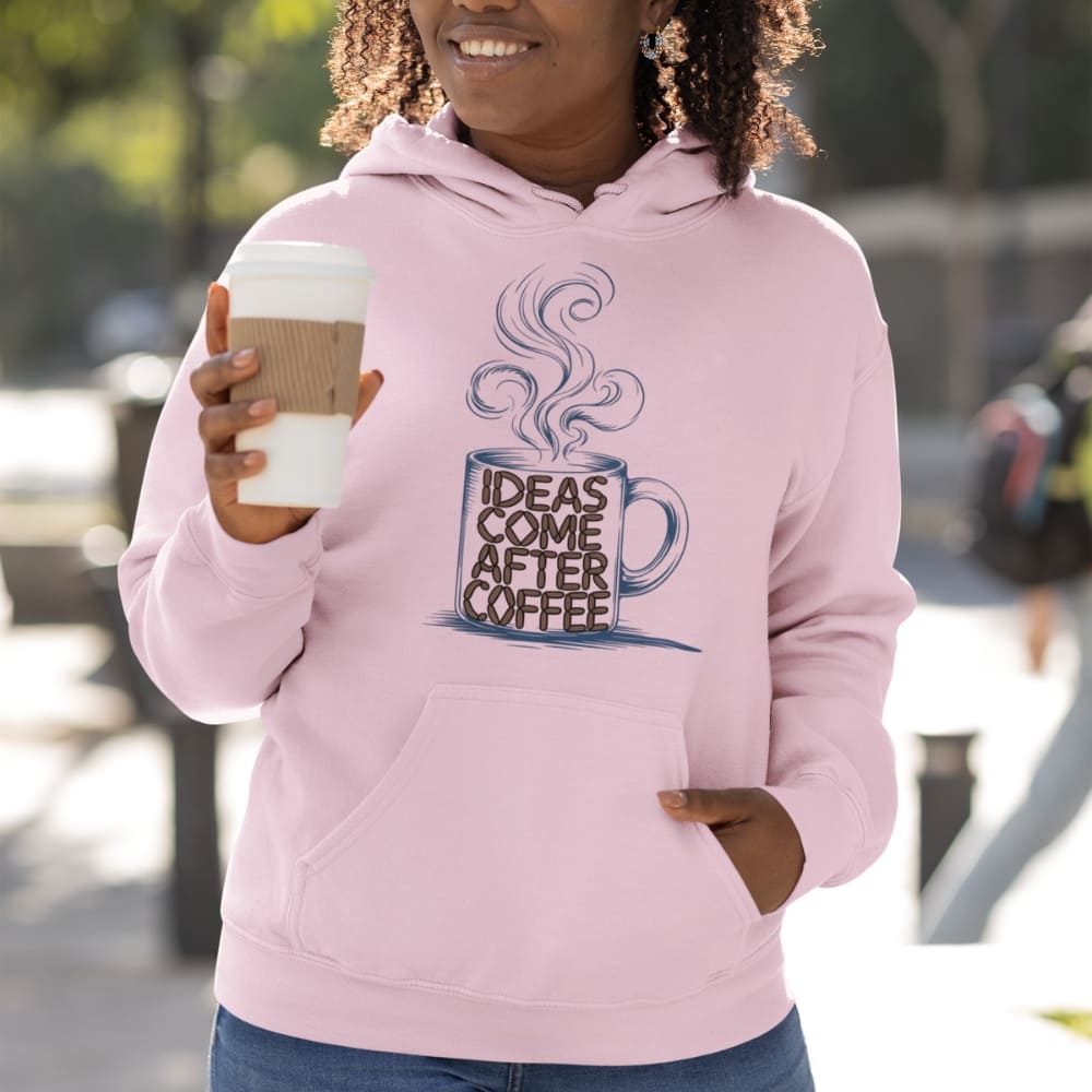 Person wearing a pink hoodie with a coffee-themed design, holding a coffee cup outdoors.