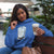 Woman wearing a blue hoodie with a coffee-themed design, holding a coffee cup outdoors.