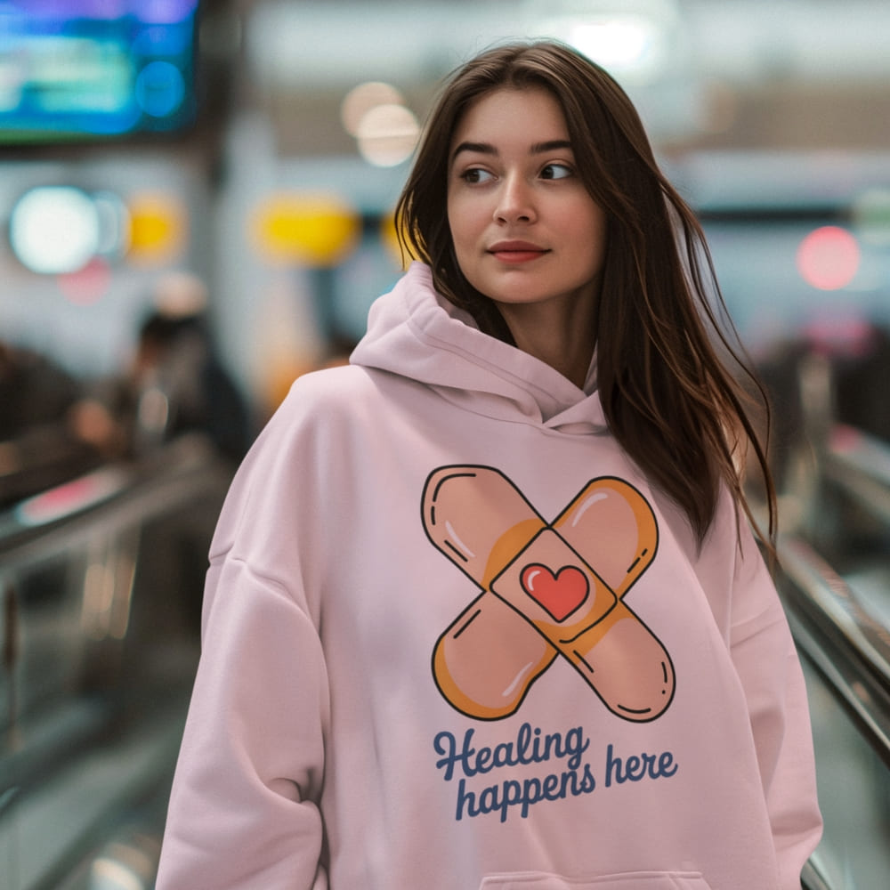 Woman wearing a pink hoodie with a bandage design and text in an indoor setting