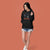 Woman wearing a black hoodie with text and graphics on an orange background