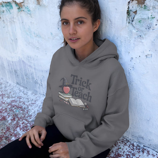 Person wearing a gray hoodie with 'Trick or Teach' design against a textured white wall.