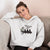 Woman wearing a white hoodie with a graphic design sitting on a couch.