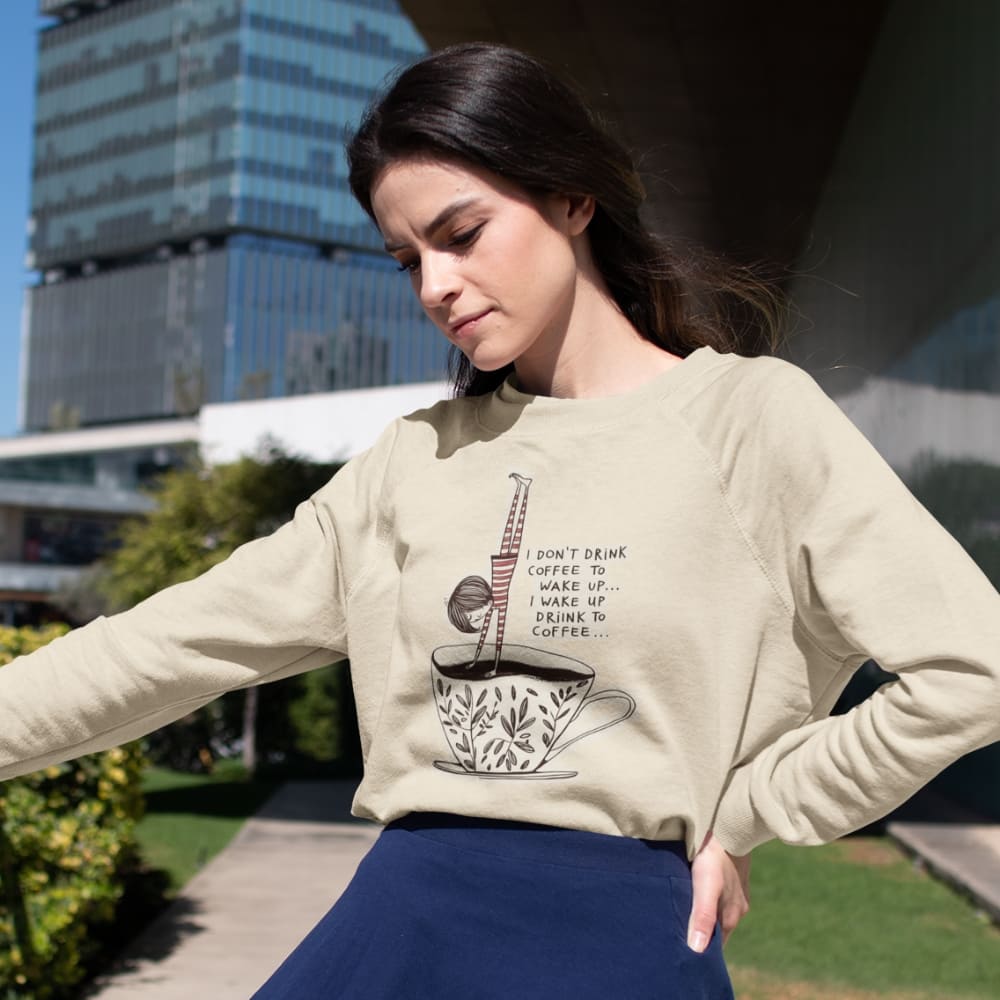 Woman wearing a beige sweatshirt with a coffee-themed design outdoors.