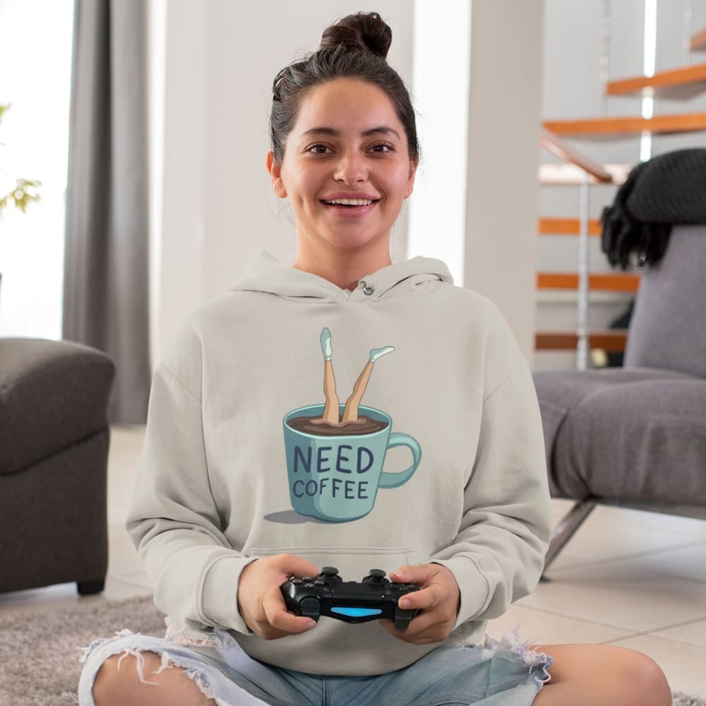 Person wearing a hoodie with a coffee-themed design, holding a gaming controller in a living room.