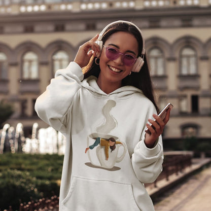 Woman wearing a white hoodie with a graphic design, pink headphones, and holding a phone outdoors.