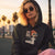 Person wearing a hoodie with a graphic design of a woman and text 'CEO of the Boo Crew' against a palm tree-lined street.