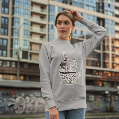 Woman wearing a gray sweatshirt with a coffee-themed design in an urban setting