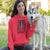 Person wearing a red hoodie with a graphic design, sitting next to a dog outdoors.