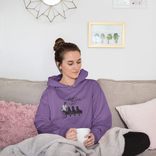 Woman wearing a purple hoodie with a graphic design, sitting on a couch holding a mug.