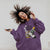 Person wearing a purple hoodie with graphic design on a plain background
