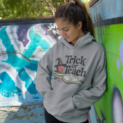 Person wearing a hoodie with 'Trick or Teach' design against a graffiti-covered wall.