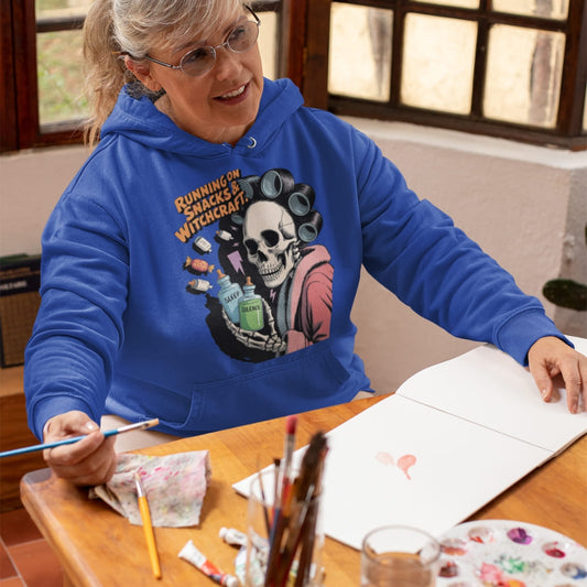 Person wearing a blue hoodie with a skull design, sitting at a table with art supplies.