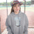 Person wearing a gray hoodie with a graphic design and colorful hat outdoors.