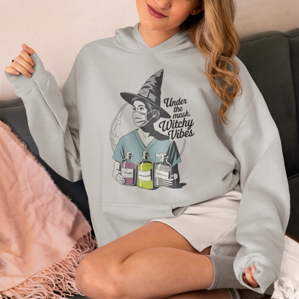 Person wearing a light gray hoodie with a graphic design of a witch holding potion bottles and text 'Under the Warm Witchy Vibes'.