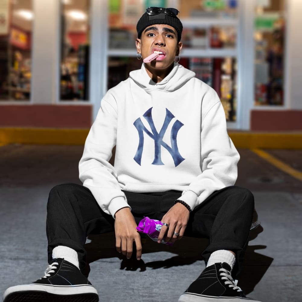 Person wearing a white hoodie with a logo, sitting on the ground in an urban setting.