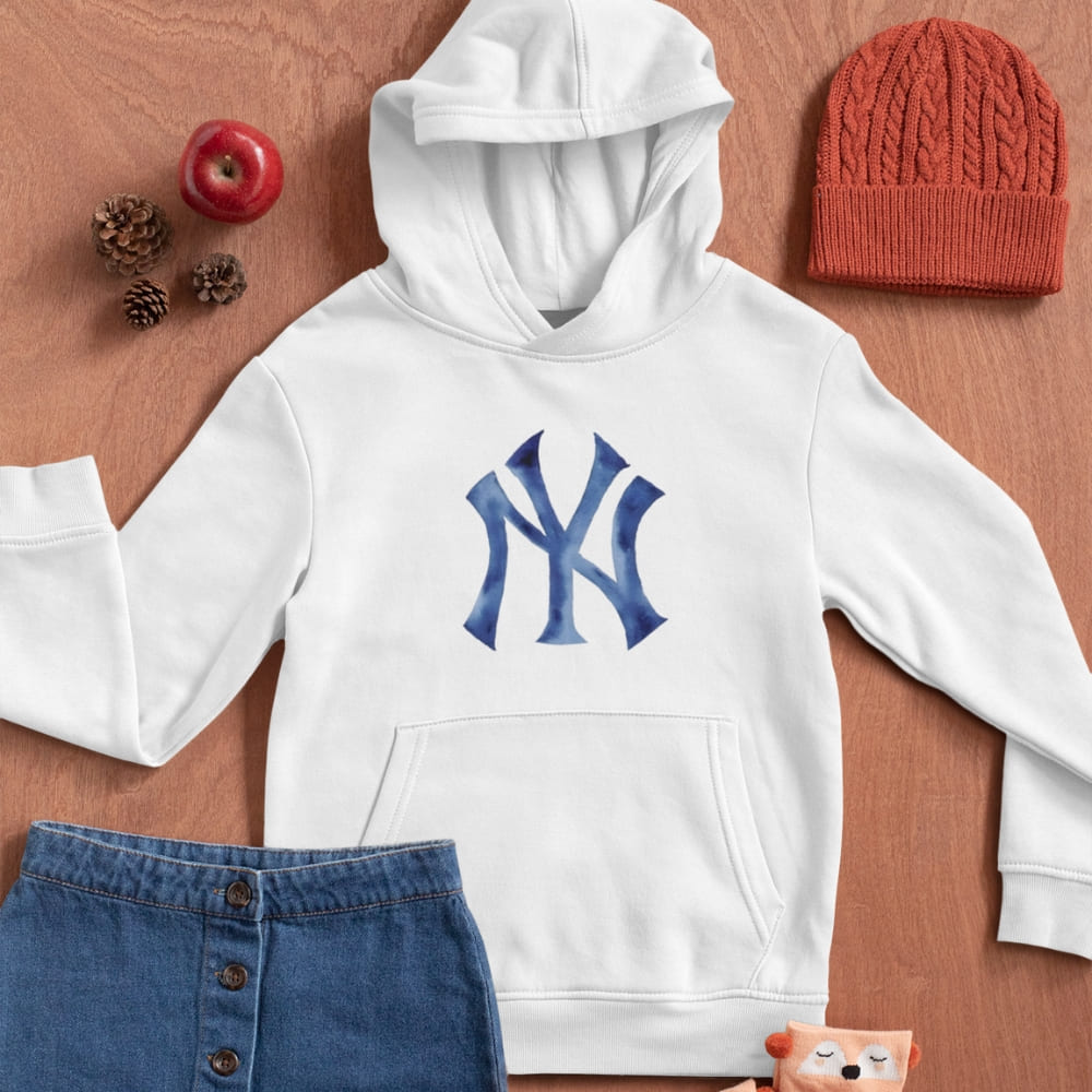 White hoodie with blue logo, red beanie, and blue denim skirt on a wooden surface.