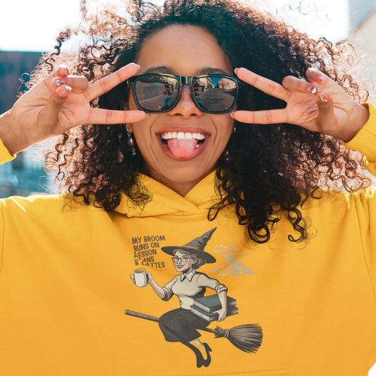 Person wearing a yellow hoodie with a witch graphic and text, making peace signs.