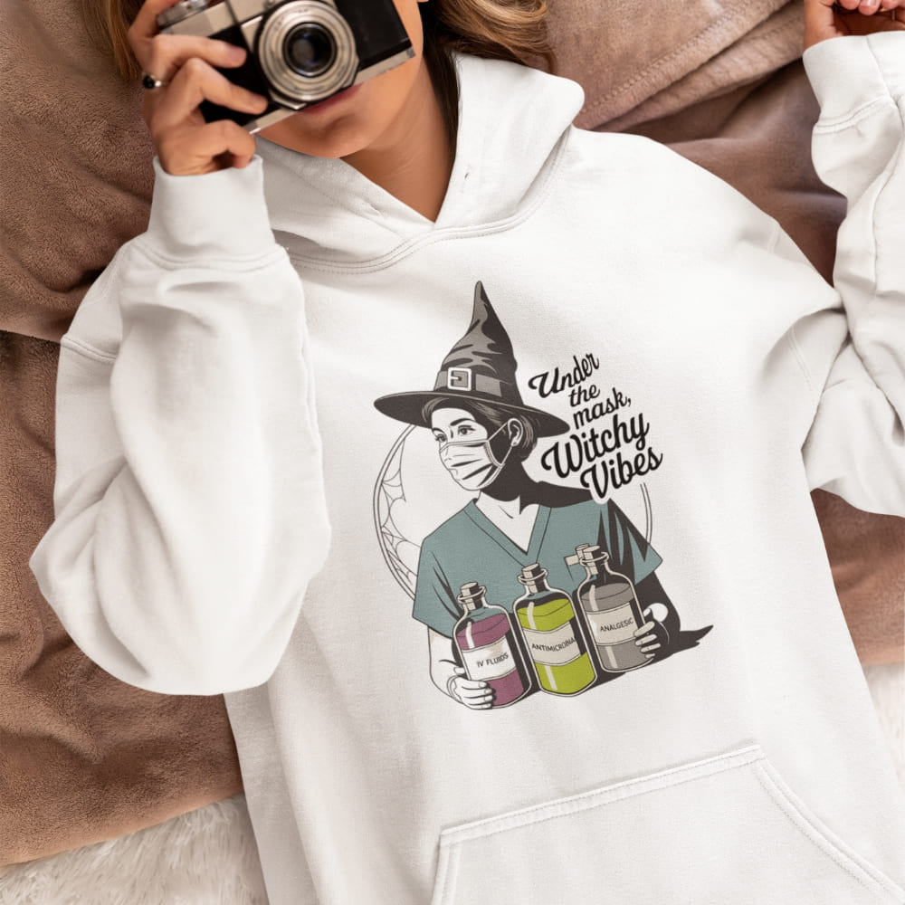 White hoodie with a graphic design of a person wearing a witch hat and face mask, holding potion bottles, with text 'Under the mask, Witty Vibes'.