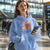 Woman wearing a blue hoodie with a graphic design, holding a phone in an indoor setting.