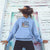 Person wearing a blue hoodie with 'Trick or Teach' design against a colorful wall.