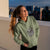 Woman wearing a green hoodie with a spider graphic on a rooftop at dusk.