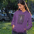 Woman wearing a purple hoodie with a graphic design and text in an outdoor setting