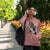 Woman wearing a pink hoodie with graphic design, headphones, and a black bag outdoors.