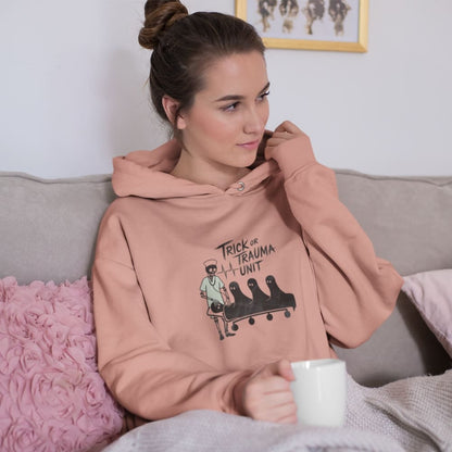 Woman wearing a pink hoodie with a graphic design, sitting on a couch holding a mug.