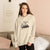 Woman wearing a beige hoodie with graphic design in a living room setting