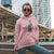 Woman wearing a pink hoodie with graphic design and text, standing in an urban setting.