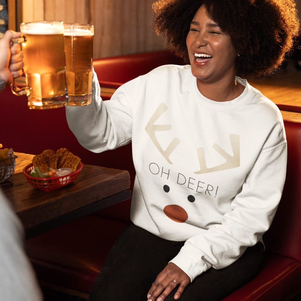Person wearing a white sweater with a reindeer design, holding two mugs of beer in a casual setting.