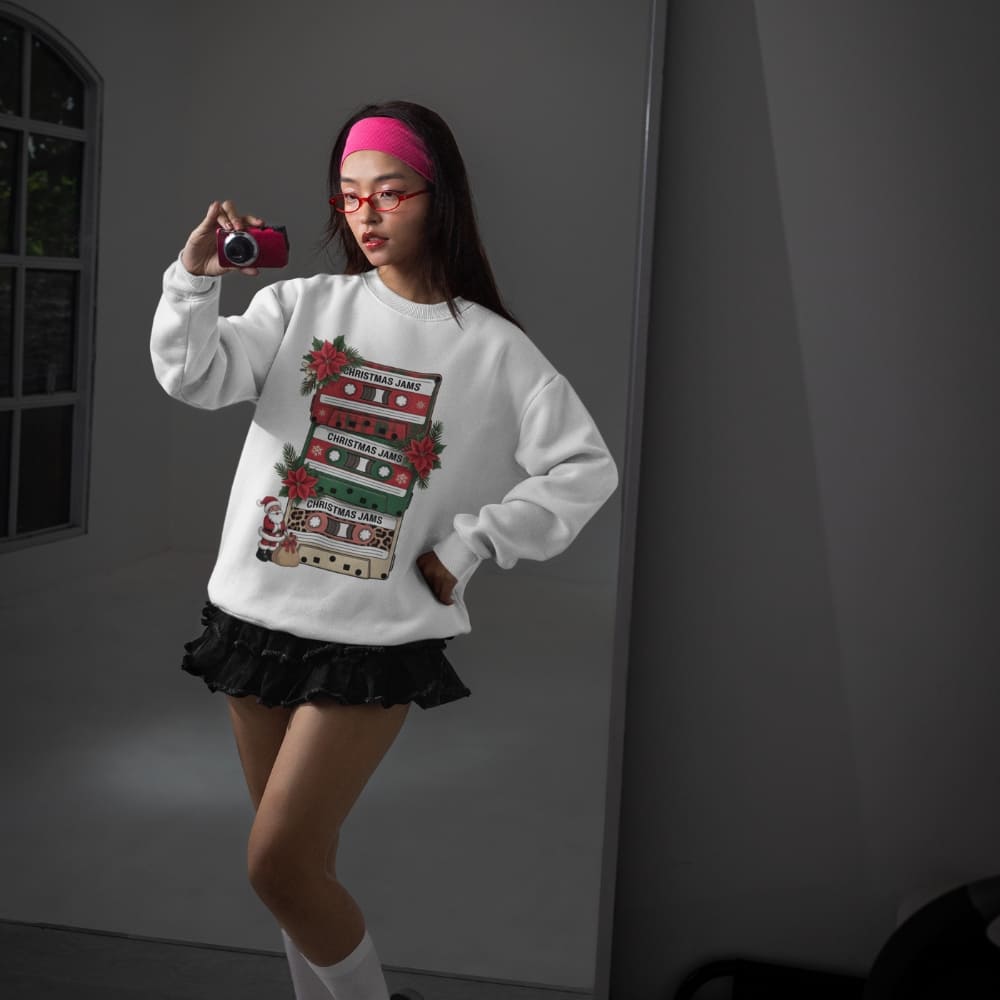 Person wearing a white sweatshirt with a festive design, taking a selfie in a dimly lit room.