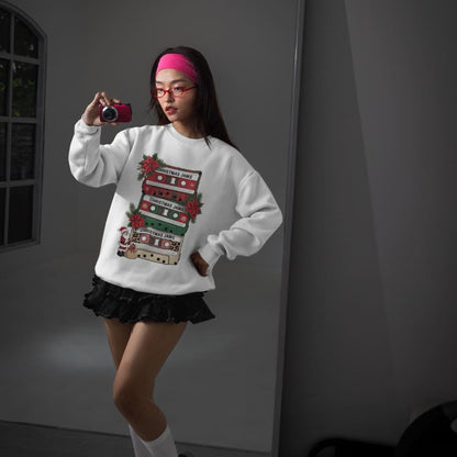 Person wearing a white sweatshirt with a festive design, taking a selfie in a dimly lit room.