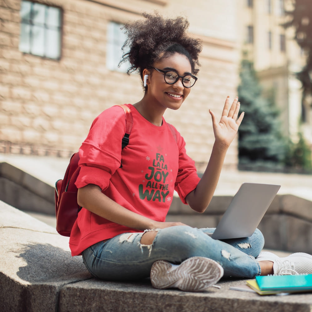 Young woman sitting outdoors with a laptop, wearing a red shirt and glasses.