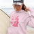 Person wearing a pink hoodie with a graphic design, standing by a body of water.