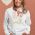 Person wearing a white hoodie with a graphic design and text on a brown background