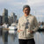 Person wearing a hoodie with a graphic design in front of a waterfront cityscape