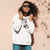 Woman wearing a white hoodie with a graphic design, standing against a beige wall.