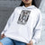 Person wearing a white hoodie with a graphic design and text against a gray wall.