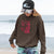 Person wearing a brown hoodie with a red graphic and a black cap on a beach.