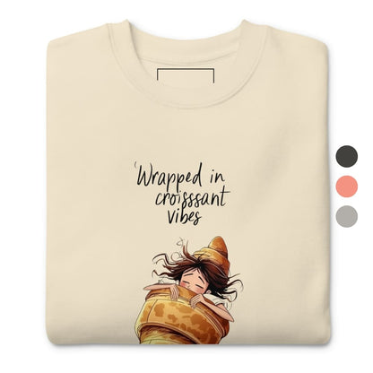 Beige t-shirt with cartoon character wrapped in a croissant and text 'Wrapped in croissant vibes' on a white background.