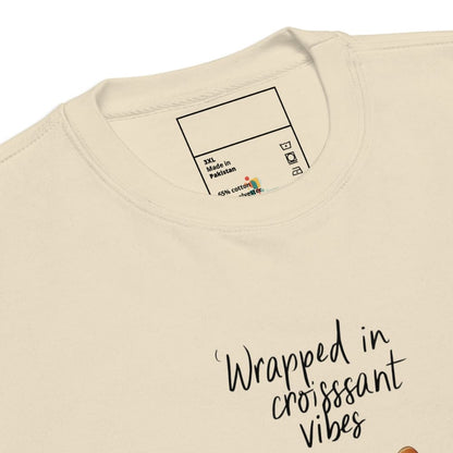 Beige sweatshirt with text 'Wrapped in croissant vibes' and a label on the collar.