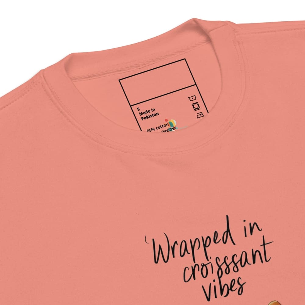 Pink t-shirt with 'Wrapped in croissant vibes' text and brand label on a white background