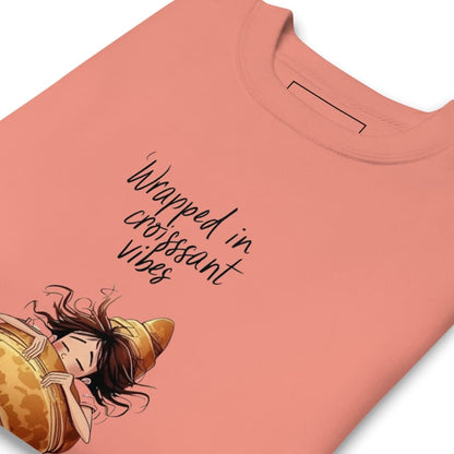 Pink t-shirt with a cartoon character and text 'Wrapped in croissant vibes' on a white background