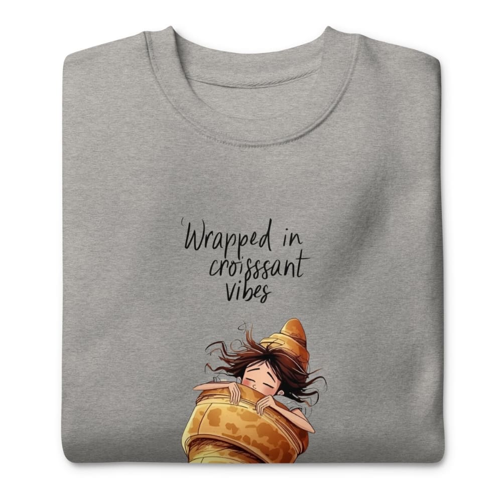 Gray t-shirt with an illustration of a person wrapped in a croissant and text 'Wrapped in croissant vibes' on a white background.