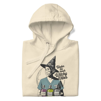 Beige hoodie with a graphic of a witch wearing a mask and text 'Under the mask, Witchy Vibes' on a white background.