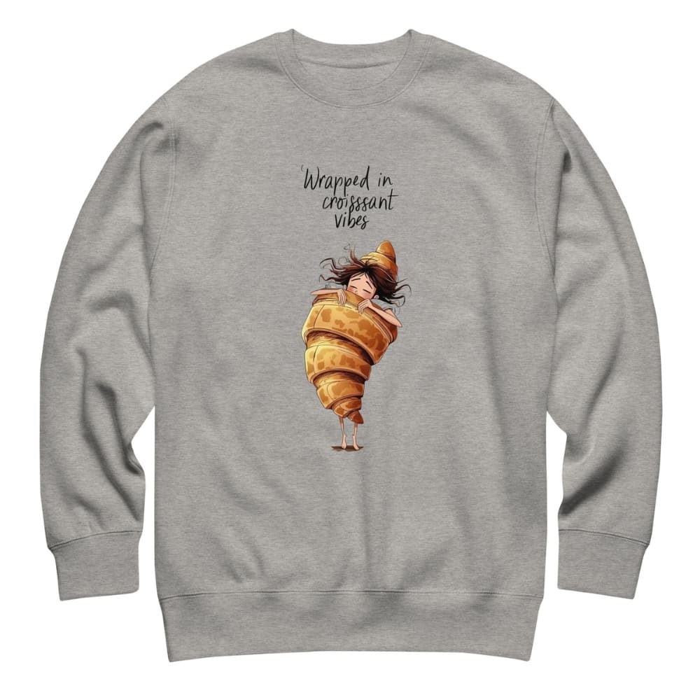 Gray sweatshirt with a cartoon character wrapped in a croissant and text 'Wrapped in croissant vibes' on a white background