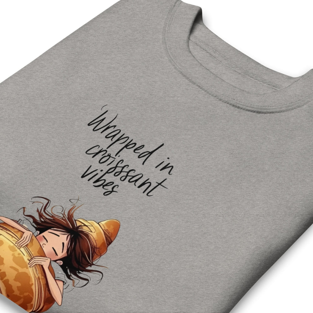 Gray t-shirt with an illustration of a person in a croissant and text 'Wrapped in croissamt vibes' on a white background.